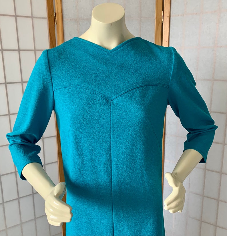 May include: A teal blue, long-sleeved dress with a V-neckline and a textured fabric.