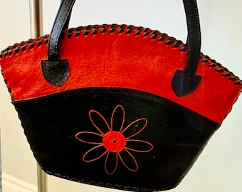 May include: A black and red leather handbag with a flower design. The bag has a stitched edge and two black leather handles.