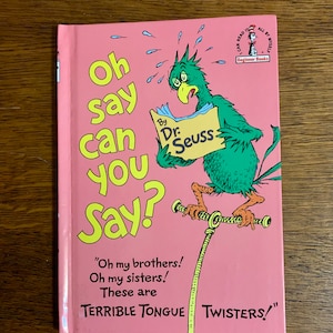 May include: A pink children's book titled "Oh Say Can You Say?" by Dr. Seuss. The cover features a green bird-like creature reading a sign. The book is part of the Beginner Books series.