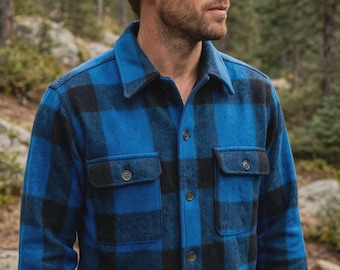 May include: A long-sleeve button-up shirt featuring a bold blue and black buffalo plaid pattern. The shirt is constructed with a classic collar, a front button placket, and two chest pockets with buttoned flaps, showcasing a textured fabric finish.