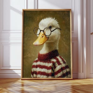 Op de afbeelding: Ingelijst kunstwerk met een eend met een ronde bril en een rood-witte gestreepte trui. De eend heeft een gele snavel en staat tegen een gedempte groene achtergrond. Het kunstwerk zit in een houten lijst.