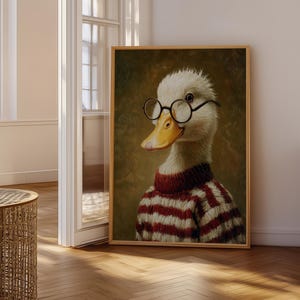 Op de afbeelding: Een ingelijst portret van een eend met een ronde bril en een rood-witte gestreepte trui. De eend heeft een gele snavel en staat tegen een donkere, getextureerde achtergrond. Het kunstwerk wordt tentoongesteld in een lichte kamer met houten vloeren.