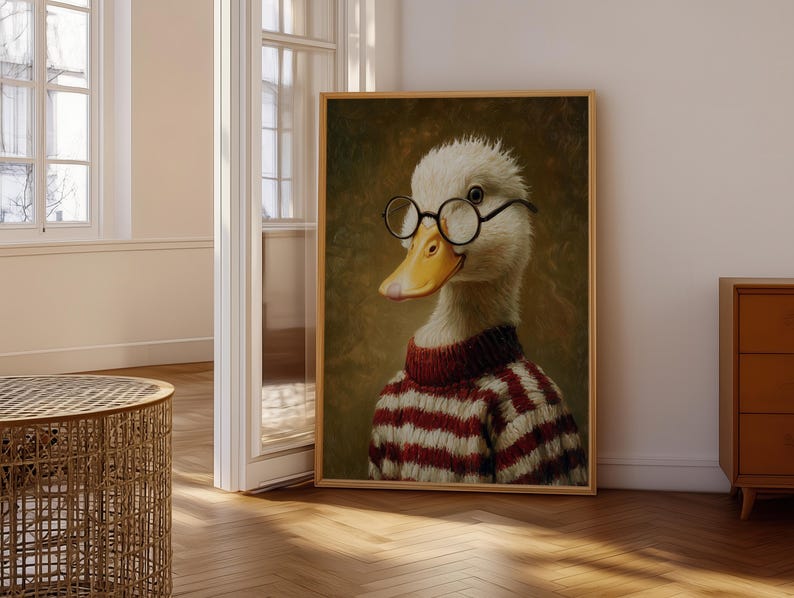 Op de afbeelding: Een ingelijst portret van een eend met een ronde bril en een rood-witte gestreepte trui. De eend heeft een gele snavel en staat tegen een donkere, getextureerde achtergrond. Het kunstwerk wordt tentoongesteld in een lichte kamer met houten vloeren.