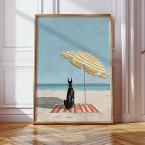 May include: Framed art print featuring a black dog sitting on a red and white striped beach towel under a yellow and white striped beach umbrella. The background shows a blue sky and ocean. The artwork is in a gold frame.