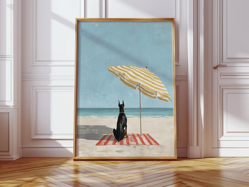 May include: Framed art print featuring a black dog sitting on a red and white striped beach towel under a yellow and white striped beach umbrella. The background shows a blue sky and ocean. The artwork is in a gold frame.