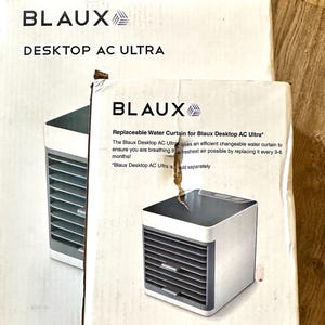 Puede incluir: Dos cajas blancas con el texto "BLAUX DESKTOP AC ULTRA" y "Replaceable Water Curtain for Blaux Desktop AC Ultra". Las cajas presentan una imagen de un peque&ntilde;o enfriador de aire blanco y gris.