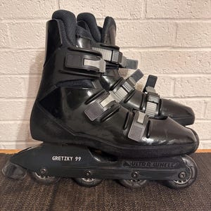 May include: Pair of black inline skates with gray buckles and the text "GRETZKY 99" on the frame. The skates have four wheels each and are designed for recreational or fitness use. The wheels are black and the boot is made of a glossy material.