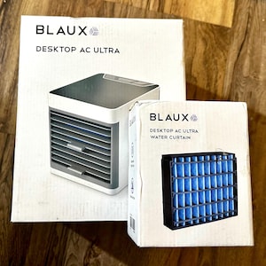 Puede incluir: Dos cajas blancas con la marca "BLAUX". Una muestra un aire acondicionado de escritorio, la otra un filtro de cortina de agua. El aire acondicionado es blanco y gris, el filtro negro con inserciones azules. El texto dice "DESKTOP AC ULTRA".