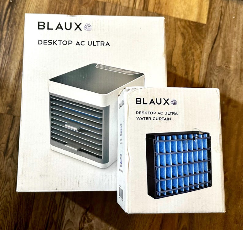 Puede incluir: Dos cajas blancas con la marca "BLAUX". Una muestra un aire acondicionado de escritorio, la otra un filtro de cortina de agua. El aire acondicionado es blanco y gris, el filtro negro con inserciones azules. El texto dice "DESKTOP AC ULTRA".