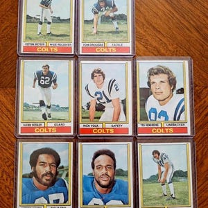 Peut inclure: Collection de neuf cartes de collection de football vintage représentant des joueurs des Colts. Chaque carte présente l'image, le nom, le poste et le nom de l'équipe du joueur. Les cartes sont dans des pochettes de protection.