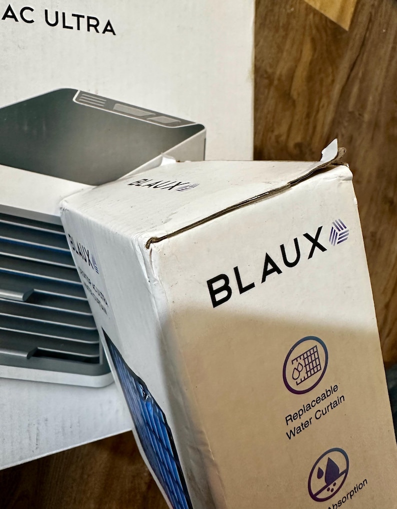 Puede incluir: Una caja de cart&oacute;n blanca con el nombre de la marca "BLAUX" en letras negras en negrita. La caja tambi&eacute;n presenta el texto "Replaceable Water Curtain" y un gr&aacute;fico de una cortina de agua. Otra caja con "AC ULTRA" es parcialmente visible.