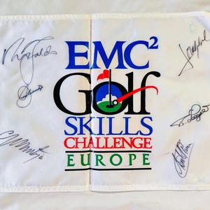 May include: White golf flag featuring the text "EMC2 Golf Skills Challenge Europe" in blue, black, red, and green. The flag has a golf ball and flag graphic and multiple signatures in black ink.
