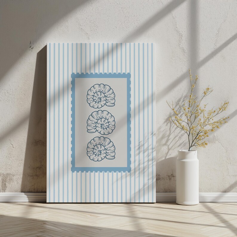 May include: A framed canvas art print featuring a blue and white striped background with a light blue postage stamp design. The stamp contains three detailed illustrations of nautilus shells in a dark blue color. The artwork is leaning against a white wall.