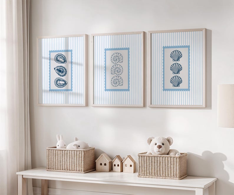 May include: Three framed prints with a nautical theme. Each print features a different seashell design in blue against a striped background. The frames are light wood. Below, two wicker baskets hold stuffed animals and miniature wooden houses.