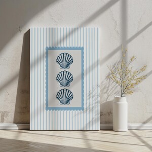 May include: A framed canvas art print featuring three stylized seashell illustrations in a vertical arrangement. The seashells are navy blue on a light beige background, framed by a light blue border. The background has light blue vertical stripes.