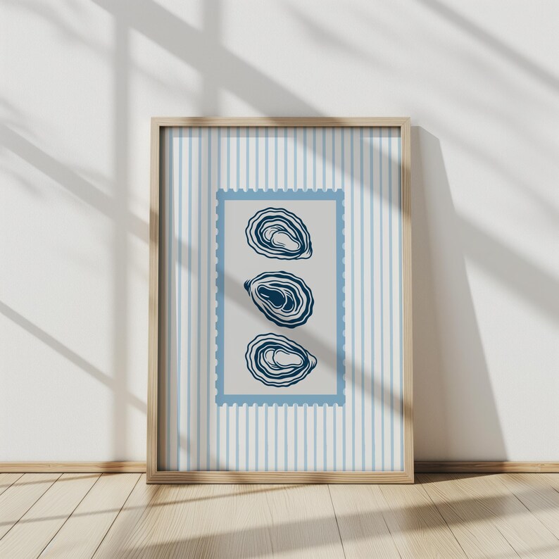 May include: A framed print featuring three stylized oyster illustrations in navy blue. The artwork is set against a light gray background within a blue postage stamp-like border, and a light blue and white striped background. The frame is made of light wood.