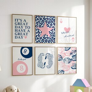 May include: A collection of six framed art prints with gold frames. The prints feature various designs, including text, a star, playing cards, a pool ball, cheetahs, and lips. The color palette includes pink, blue, and white.