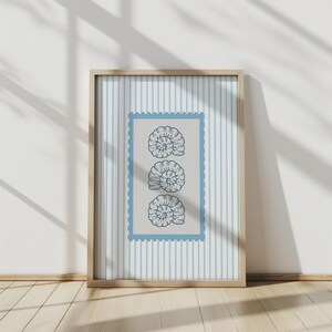 May include: A framed print featuring three stylized nautilus shell illustrations in a vertical arrangement. The shells are dark blue on a light gray background within a blue postage stamp-style border. The background has vertical blue stripes.