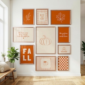 Könnte beinhalten: Ein Galerie-Wandset aus elf gerahmten Drucken mit herbstlichen Motiven in Orange und Creme. Die Designs zeigen einen Kürbis, ein Ahornblatt, eine Kaffeetasse, ein Karomuster und Texte wie "FALL", "Harvest blessings" und "Sweater Weather".