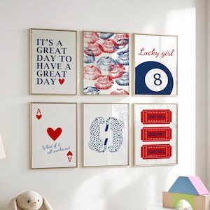 May include: A collection of six framed art prints with gold frames. The prints feature various designs, including text, lips, an eight ball, playing cards, cheetahs, and tickets. The color palette includes red, blue, and white.