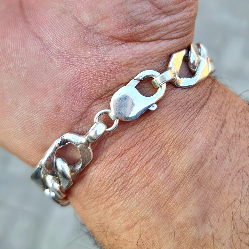 May include: A silver chain bracelet with a lobster clasp closure. The bracelet is made of thick, chunky links.