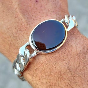 May include: A silver chain bracelet with a large oval-shaped dark brown gemstone.