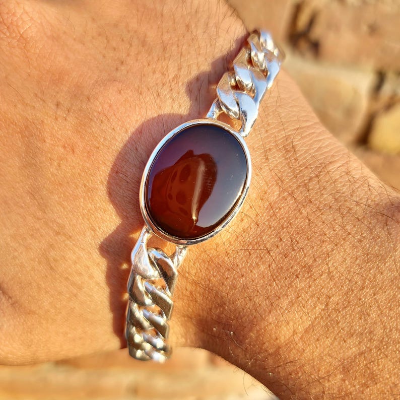 May include: A silver chain bracelet with a large, oval-shaped, dark red gemstone.