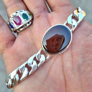 May include: A silver chain bracelet with a large oval brown agate gemstone. The bracelet has a curb chain design.