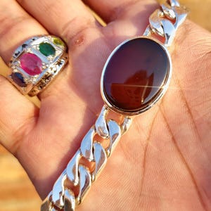 May include: A silver chain bracelet with a large, oval-shaped, dark brown gemstone. The bracelet has a curb chain design.
