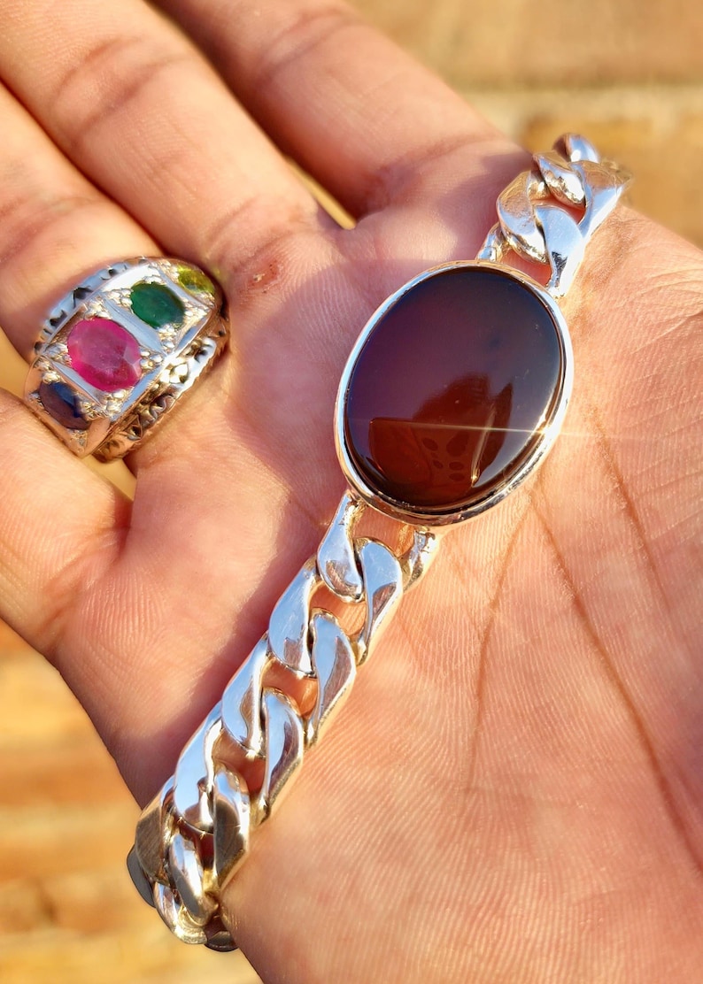 May include: A silver chain bracelet with a large, oval-shaped, dark brown gemstone. The bracelet has a curb chain design.