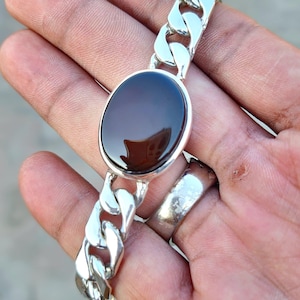 May include: A silver chain bracelet with a dark brown oval gemstone. The chain is a curb style.