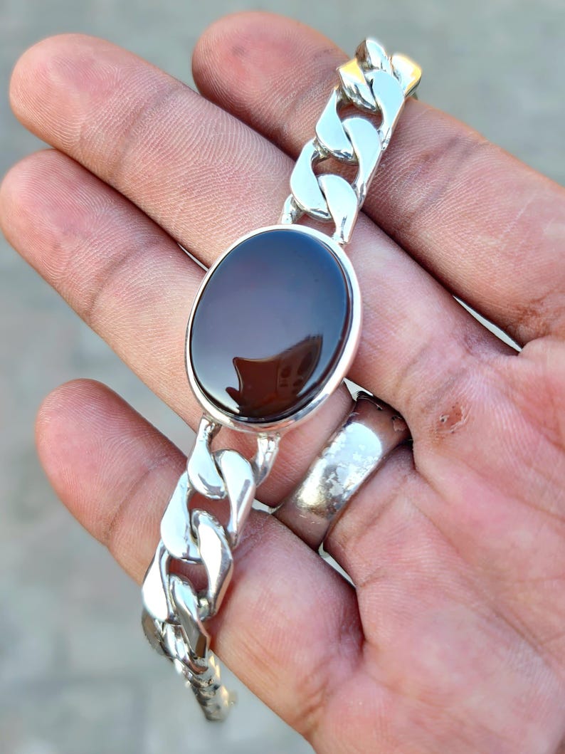 May include: A silver chain bracelet with a dark brown oval gemstone. The chain is a curb style.