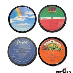Könnte beinhalten: Vier 45-U/min-Vinyl-Untersetzer mit verschiedenen Künstlern und Albumcovern. Die Untersetzer sind schwarz mit einem silbernen Rand. Der oberste Untersetzer zeigt einen Regenbogen und den Text "One More From The Road Lynyrd Skynyrd MCA Records MCA2-8011 Side 4". Der zweite Untersetzer zeigt ein grünes, rotes und weißes Design mit dem Text "Atlantic Deja Vu Crosby, Stills, Nash & Young Stereo One 50.2200". Der dritte Untersetzer zeigt ein blaues, weißes und rotes Design mit dem Text "Fantasy Stereo Presents Green River Creedence Clearwater Revival Stereo Fant 8383 Full Radial Stereo". Der vierte Untersetzer zeigt ein gelbes, oranges und grünes Design mit dem Text "Rare Earth RS 514 HL174 Stereo Ecology Rare Earth Satisfaction Guaranteed It. 4.34 Nice Place To Visit It. 3.53 Eleanor Rigby 3.28 Produced By Tom Nada Roenak Whitfield".