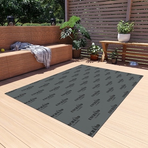 May include: A dark gray outdoor rug with the text "UNCHAND CO SUPPLY" repeated across the surface. The rug is rectangular and lies on a wooden deck, surrounded by outdoor furniture and potted plants.
