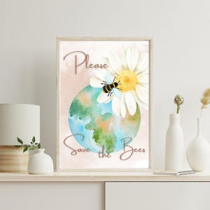May include: A framed print featuring a watercolor illustration of the Earth, a daisy, and a bee. The text "Please Save the Bees" is written in cursive. The artwork is displayed on a white surface with a lamp and vases.