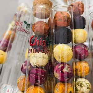May include: Clear glass tubes filled with colorful, spherical spices. The tubes are labeled "Chis and Spice". The spices range in color from yellow and orange to red and purple, with some appearing black. A cork stopper seals one tube.