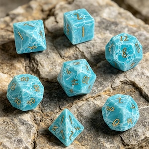 May include: A set of seven dice in different shapes, including a cube, a d20, and a d4. The dice are a marbled turquoise colour with gold-coloured numbers. The dice are on a rough, grey stone surface.
