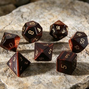 May include: Seven polyhedral dice with a dark brown, marbled effect and gold numerals. The dice are displayed on a textured, light grey stone surface. Ideal for role-playing games, the dice are a mix of shapes.