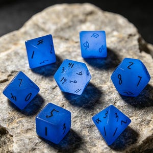 May include: A selection of blue dice with black numerals, including six-sided and multi-sided dice. The dice are displayed on a textured, grey stone surface, ideal for tabletop gaming. The dice are in various shapes.