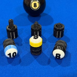 May include: A black eight ball with a white and yellow number eight. Several black pool cue tips are arranged around the ball. One tip has a blue stripe with the number ten, and another has the number eight.