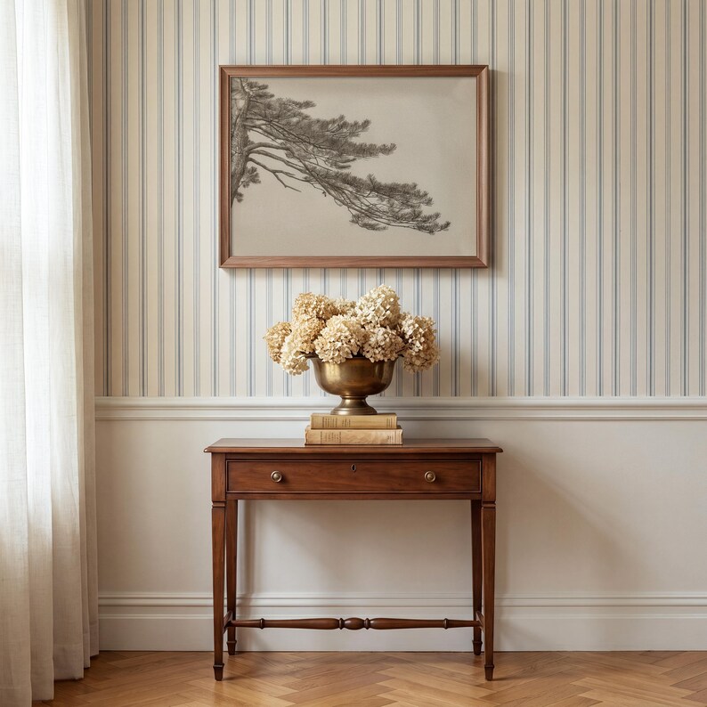 Puede incluir: Una mesa consola de madera con un caj&oacute;n y un travesa&ntilde;o inferior, coronada con un cuenco de lat&oacute;n lleno de hortensias secas y un boceto enmarcado al carboncillo de una rama de pino colgado en una pared de rayas azules y blancas.