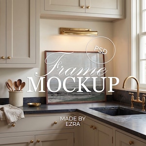 Może przedstawiać: Wnętrze kuchni z oprawionym dziełem sztuki z napisem "Frame Mockup". Grafika przedstawia krajobraz. Kuchnia posiada jasne szafki, ciemny blat i mosiężne elementy. Tekst na zdjęciu brzmi "Made by Ezra."
