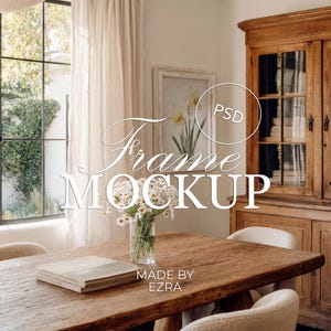 May include: A wooden dining table with a vase of daisies and a framed floral print. The text "Frame Mockup" and "Made by Ezra" are visible. The room has a window with natural light and a wooden cabinet.