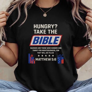 May include: Black t-shirt with the text "HUNGRY? TAKE THE BIBLE" in white, red, and blue. Below the text is "BLESSED ARE THOSE WHO HUNGER AND THIRST FOR RIGHTEOUSNESS, FOR THEY WILL BE FILLED" and "MATTHEW 5:6".