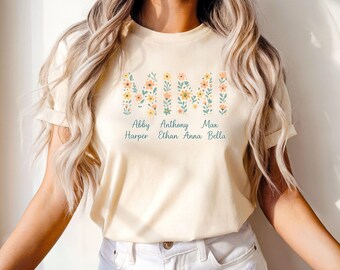 May include: A light beige t-shirt with the word "MIMI" spelled out in floral letters. The names Abby Harper, Anthony Ethan, Max Anna, and Bella are printed below the floral letters.