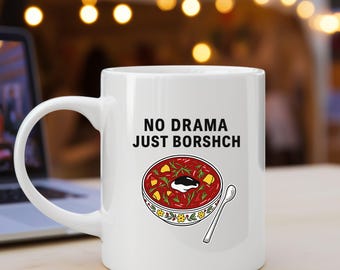 Op de afbeelding: Witte keramische mok met de tekst "NO DRAMA JUST BORSCHCH". De mok heeft een kleurrijke illustratie van een kom borsjt met een lepel. De mok heeft een groot handvat en is geschikt voor warme dranken.