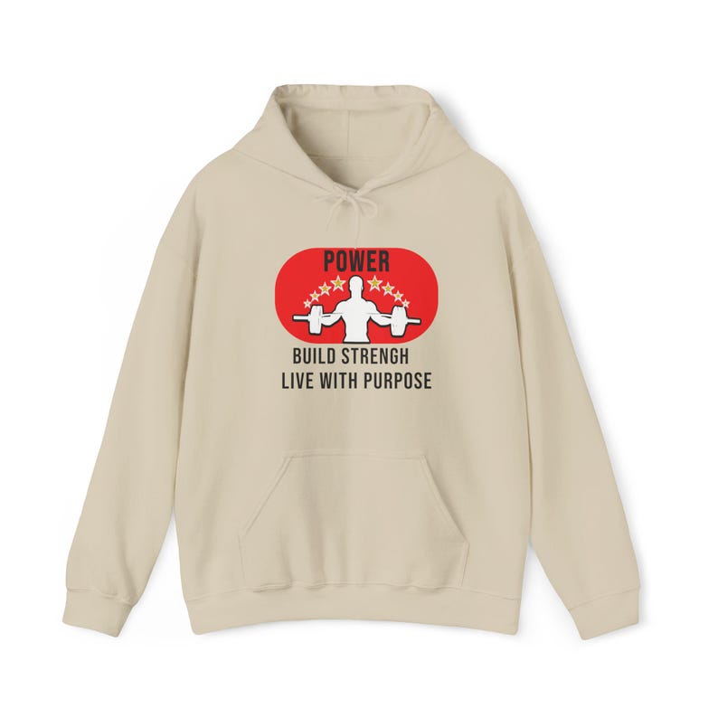 K&ouml;nnte beinhalten: Ein beigefarbener Kapuzenpullover mit einer Vordertasche und einer Kapuze mit Kordelzug. Auf der Vorderseite befindet sich ein rotes Oval mit dem Wort "POWER" &uuml;ber einer Gewichtheber-Grafik und dem Text "BUILD STRENGTH LIVE WITH PURPOSE".