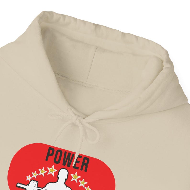 K&ouml;nnte beinhalten: Cremefarbener Kapuzenpullover mit Kordelzug und roter ovaler Grafik. Die Grafik zeigt das Wort "POWER" in Wei&szlig;, eine Gewichtheber-Silhouette und goldene Sterne. Der Hoodie ist aus weichem Material.