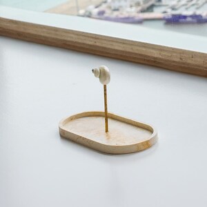 May include: A small, oval-shaped, wooden tray with a seashell on a metal stand in the center.