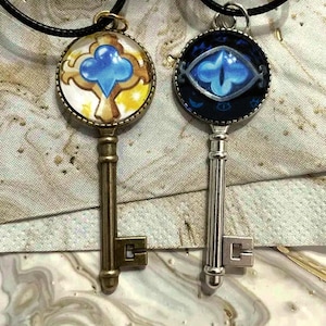 May include: Two key pendant necklaces. One key has a bronze finish with a blue and yellow design. The other key has a silver finish with a blue eye design. Both keys hang from black cords.